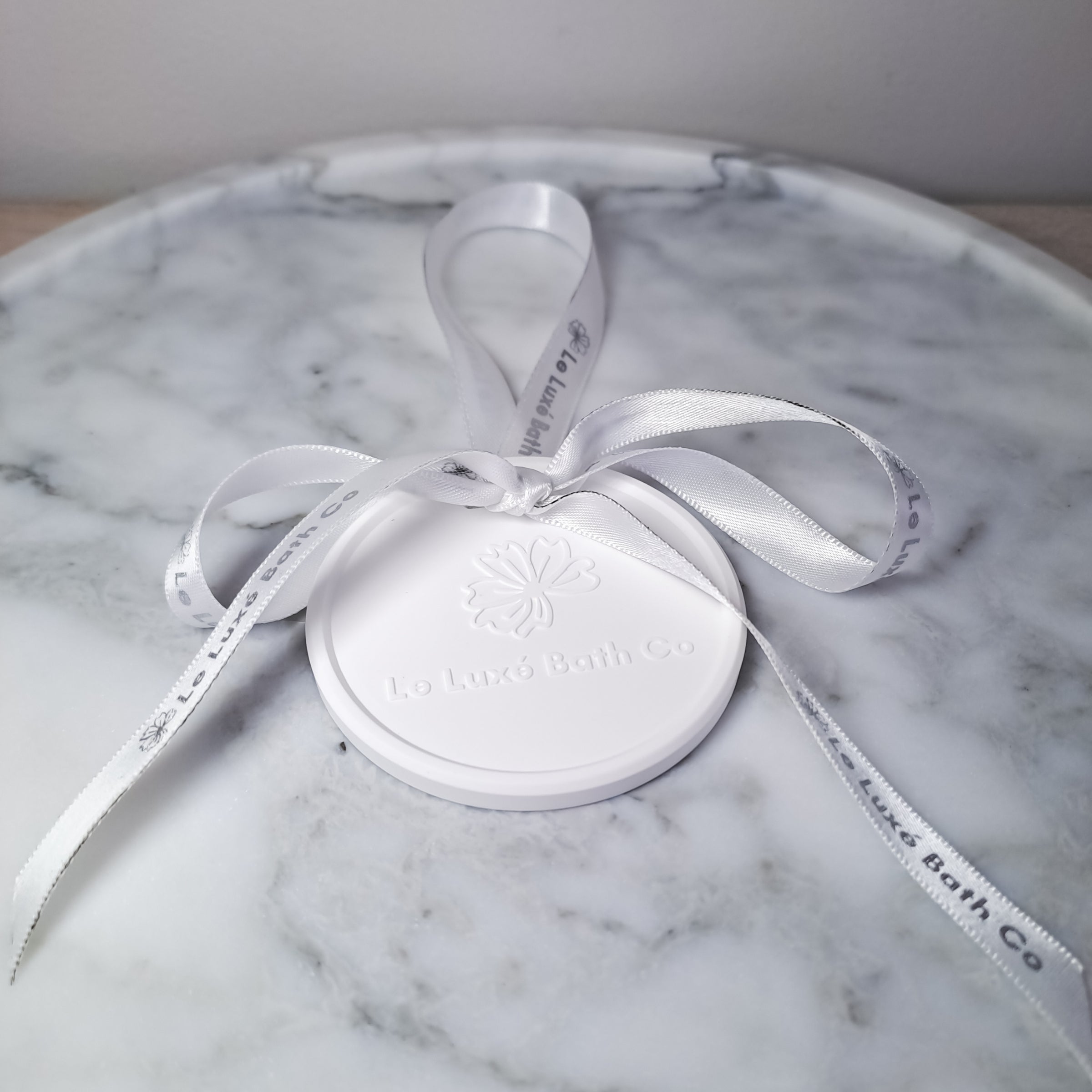 Aroma disc with white logo ribbon on marble tray on wooden surface
